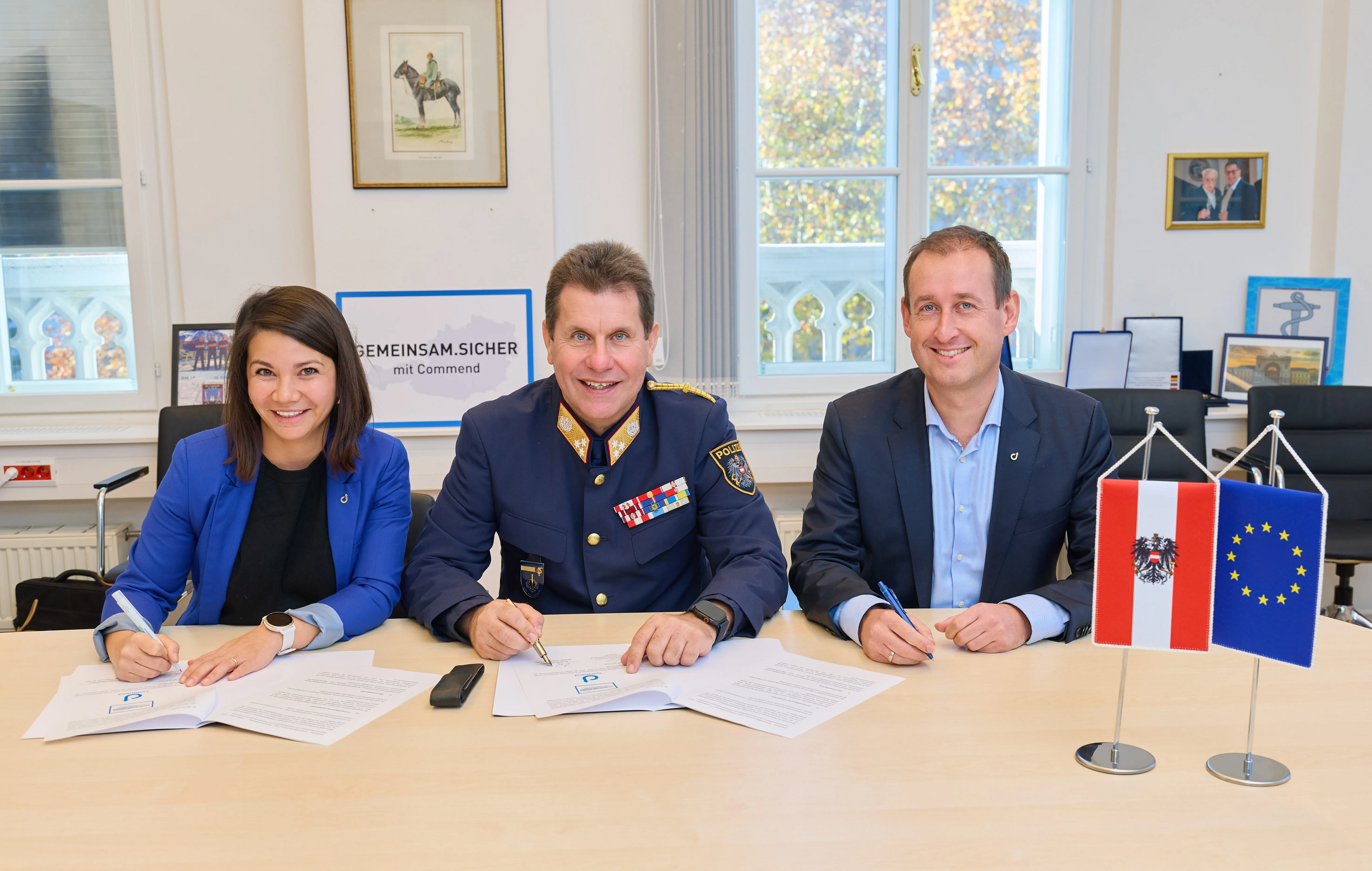 Partnership for Future Communication Three professionals sign a document with Austrian and EU flags.