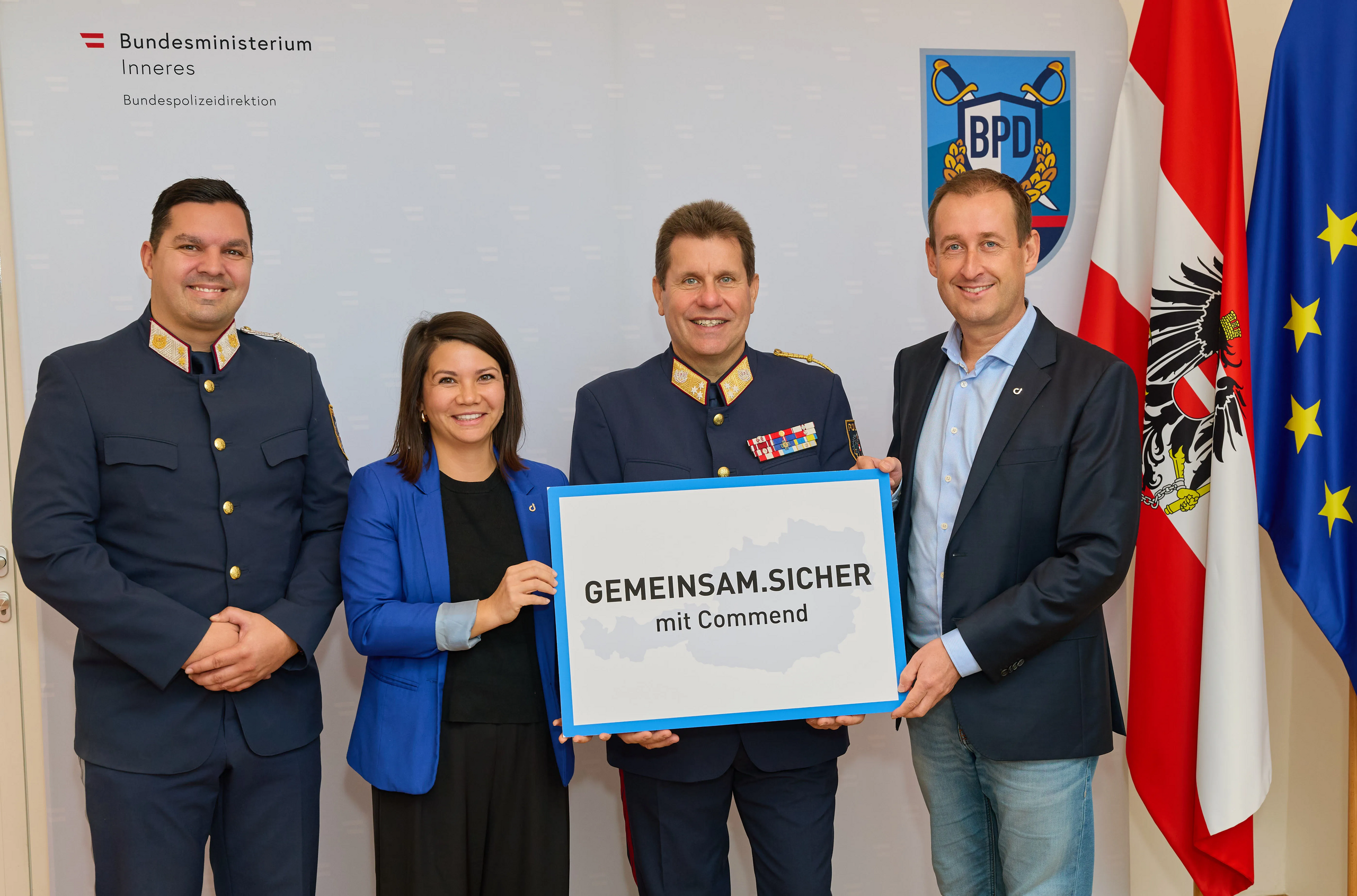 Commend & Austrian Police: Joint Security Four people, two in police uniform, holding a 'Gemeinsam.Sicher mit Commend' sign. Austrian and EU flags visible.