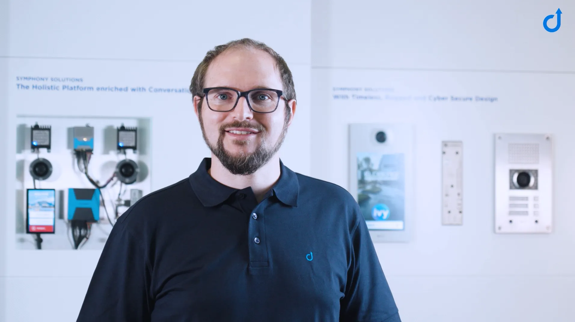 Man with Intercom & Comm Systems A smiling man in a black polo shirt, standing before a display of diverse intercom and communication systems.