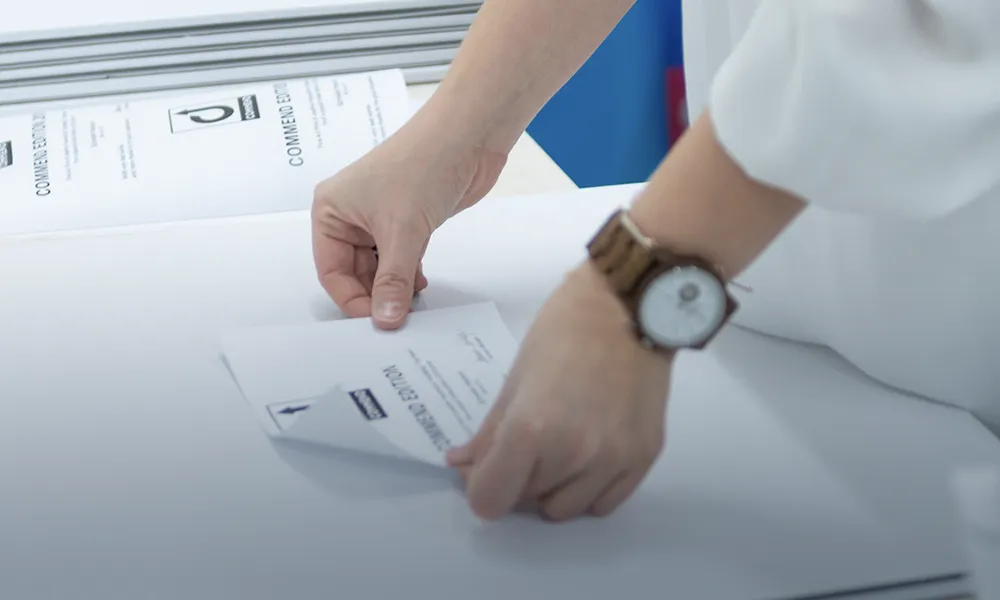 Commend Document Preparation Hands folding white documents marked "COMMEND EDITION" on a table. A wooden watch is visible.