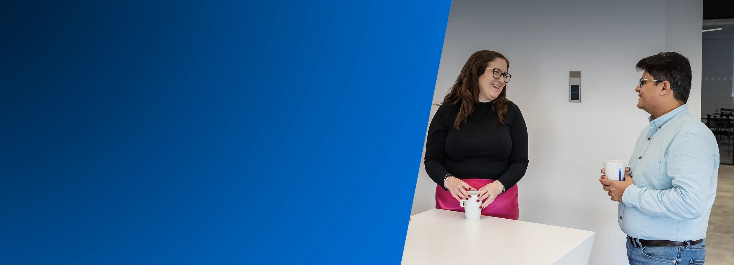 End user Two smiling office workers talk near a wall-mounted intercom system.
