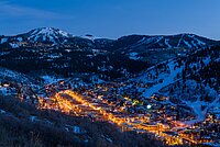Park City at Dusk, Winter Wonderland Aerial night view of a brightly lit town in a snowy mountain valley with ski slopes.